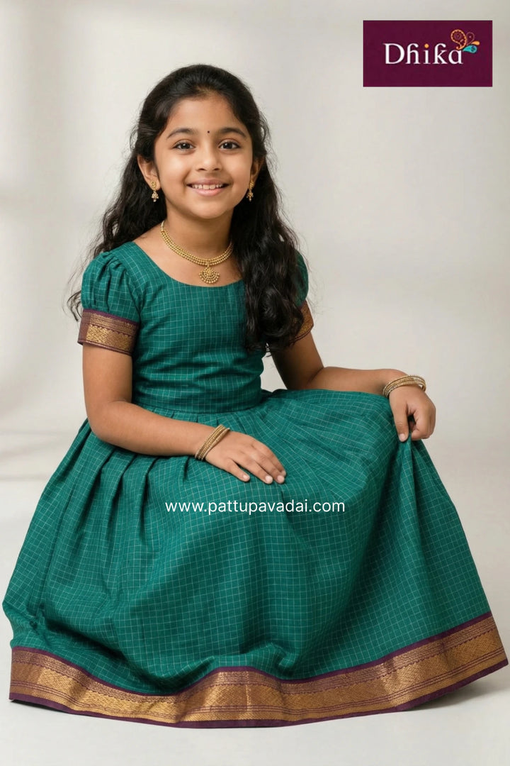Young girl wearing a green traditional outfit with gold accents, sitting on a white background.