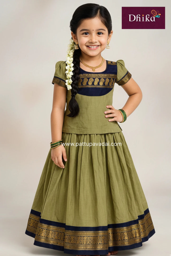 Young girl wearing a green traditional outfit with gold and navy details, smiling against a plain background.