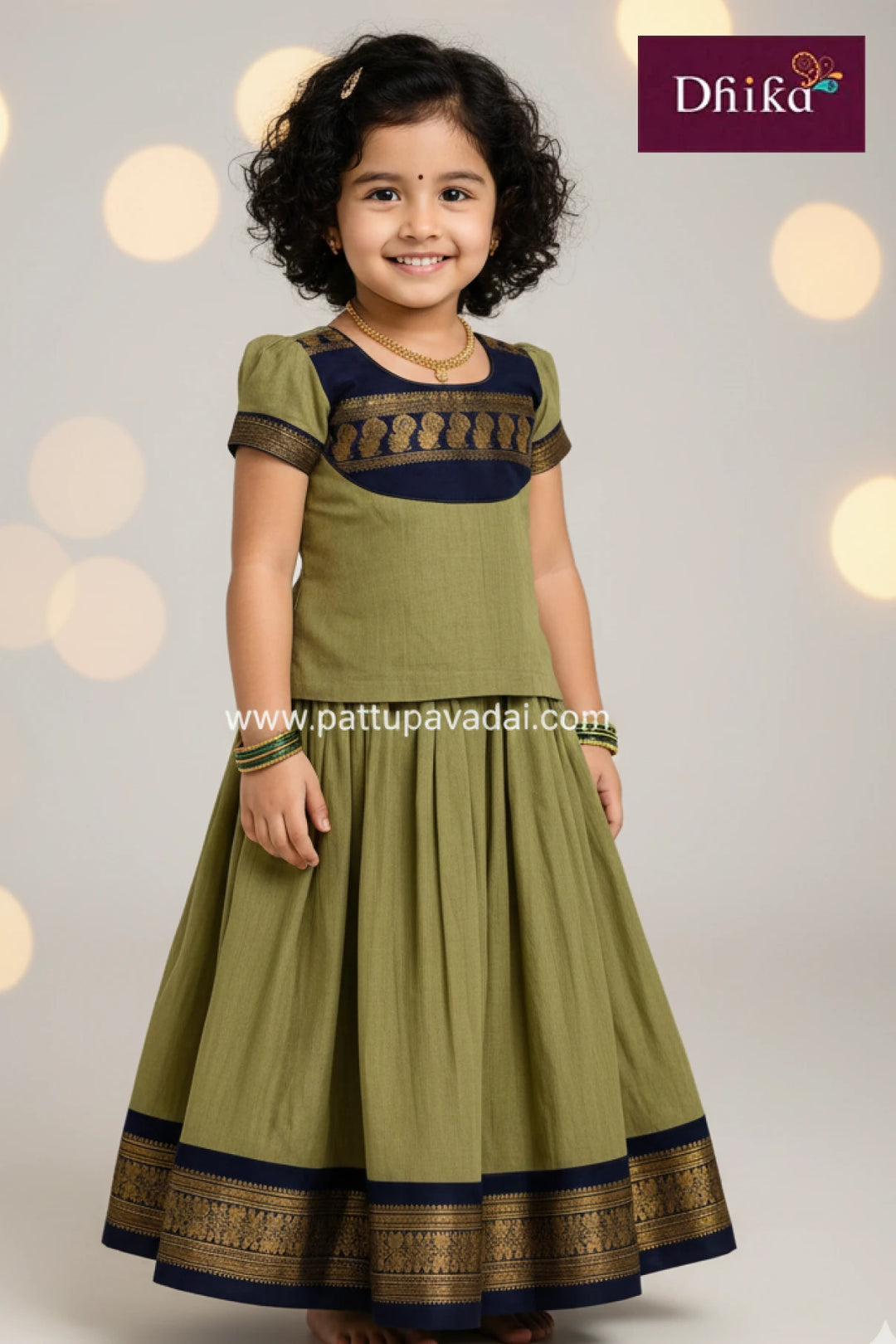 Young girl wearing a green traditional outfit with black and gold details, against a soft light background.
