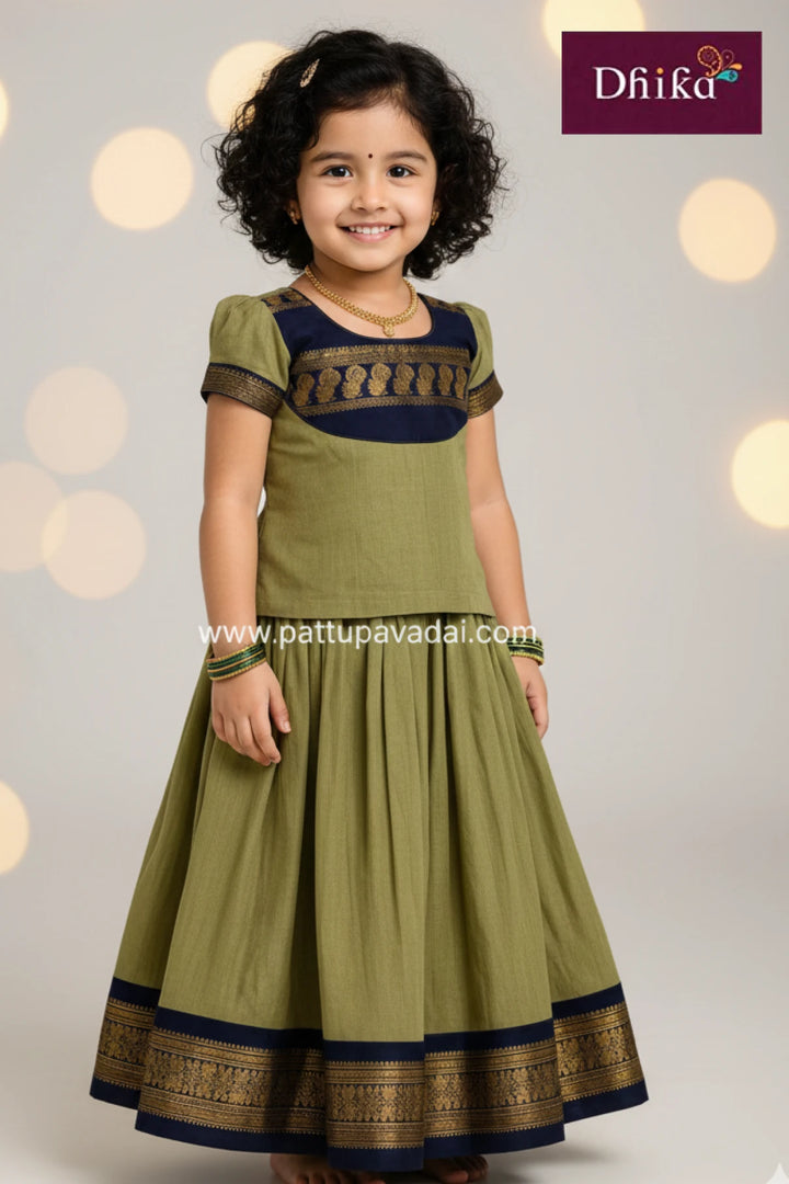 Young girl wearing a green traditional outfit with black and gold details, against a soft light background.