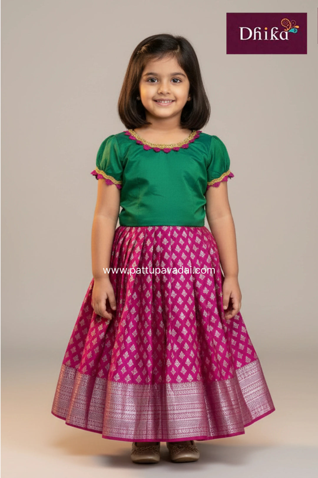 Young girl wearing a green top and pink skirt with a pattern, standing against a plain background. Brand 'Dhika' is visible.