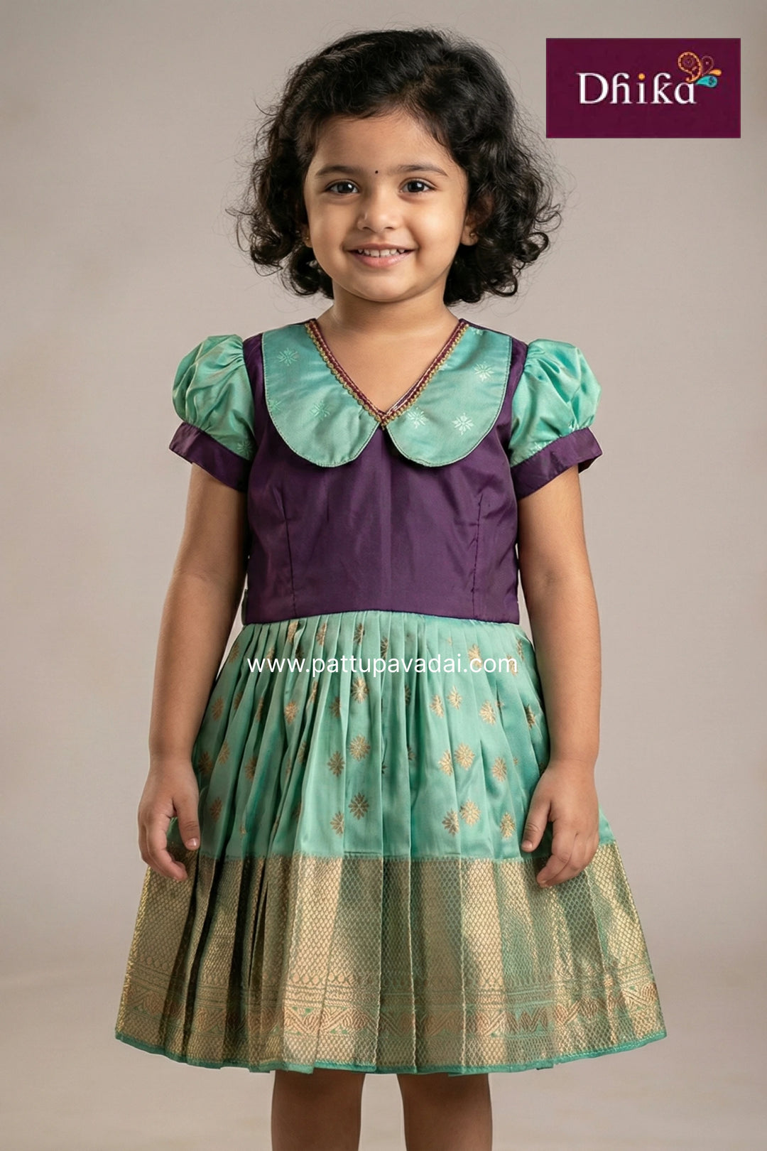 Young girl wearing a green and purple traditional outfit with 'Dhika' branding.
