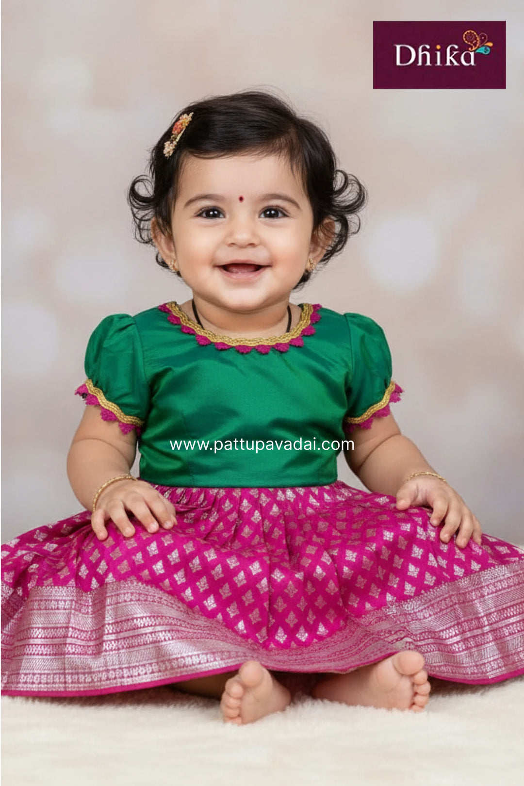 Baby wearing a green and pink traditional outfit with 'Dhika' branding.