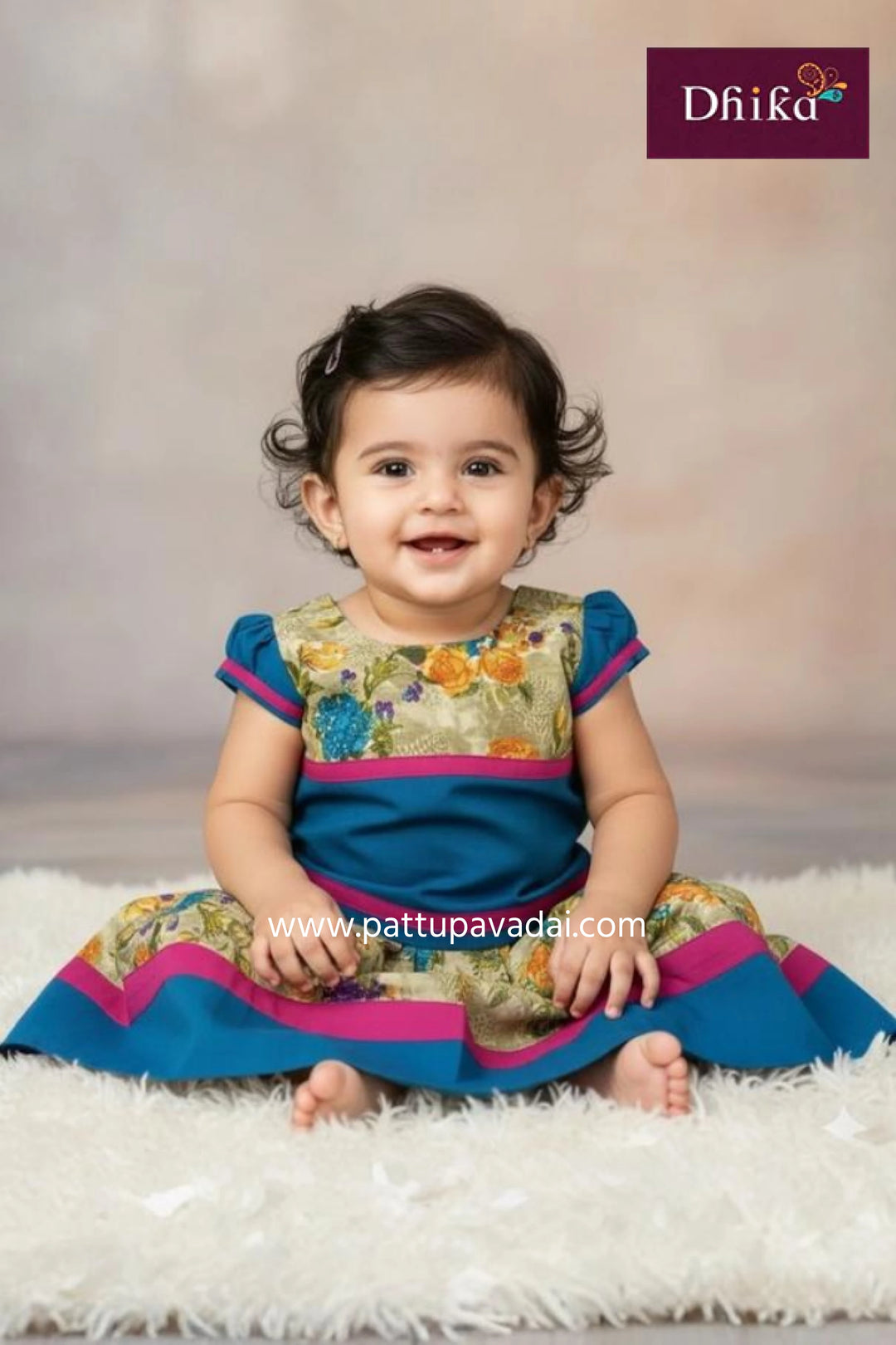 Baby wearing a colorful traditional outfit with 'Dhika' branding on a soft white background.