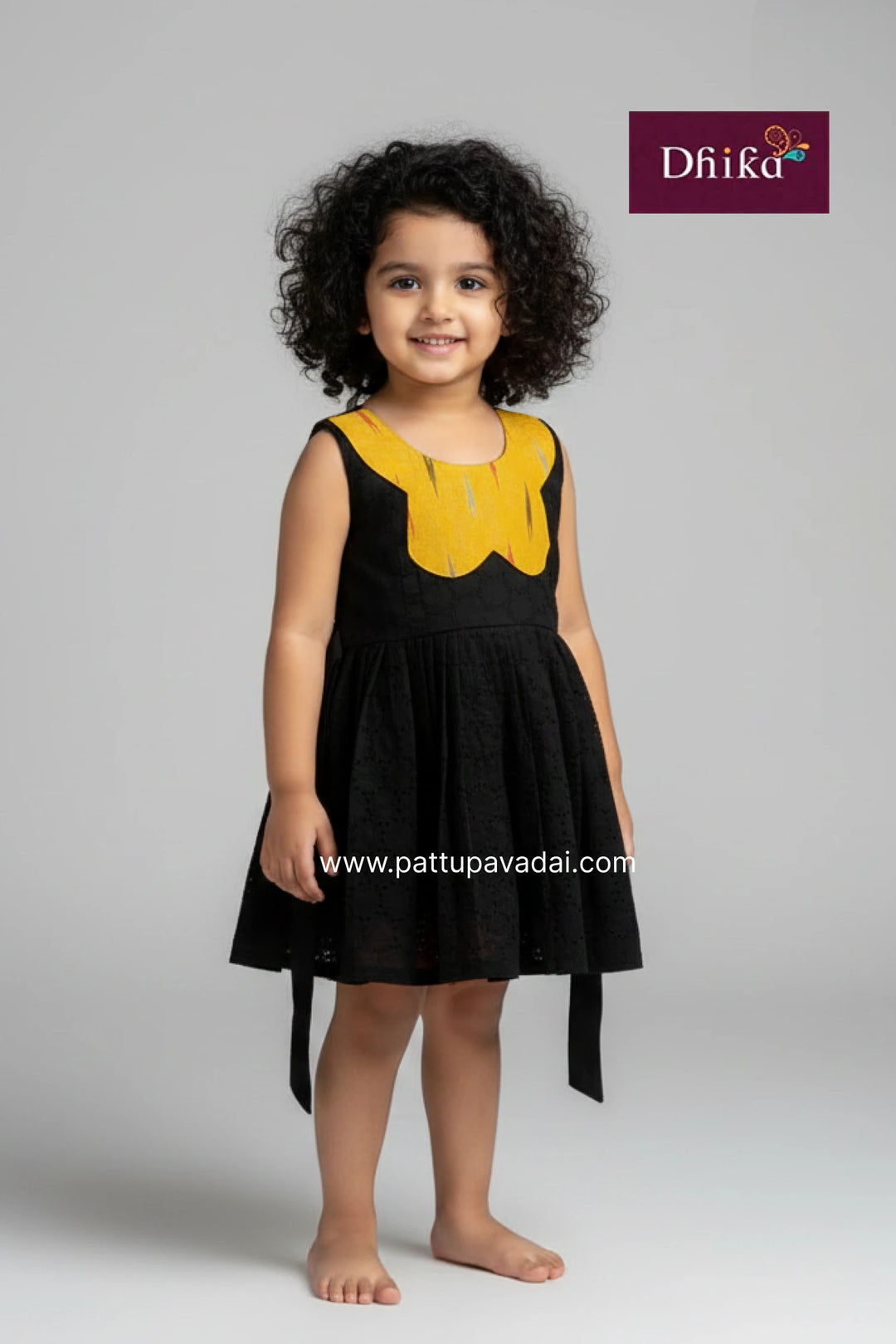 Young girl wearing a black dress with yellow accents, standing against a plain background with 'Dhika' branding.