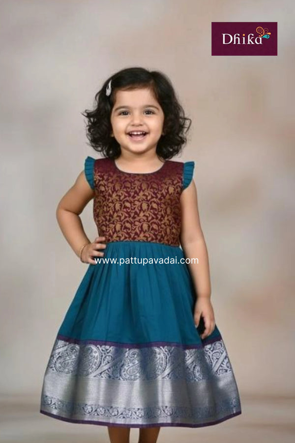 Young girl wearing a traditional dress with floral patterns, brand 'Dhika' visible.