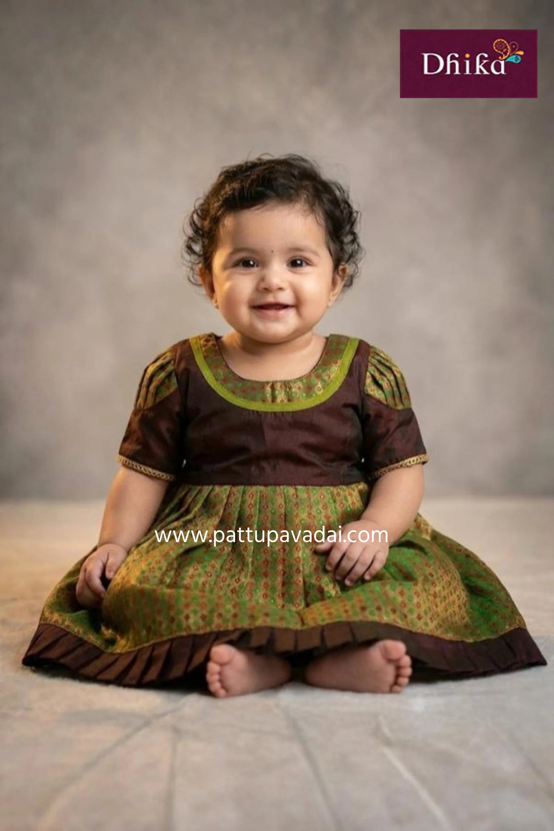 Child wearing a traditional outfit with a brown and green pattern, sitting on a light-colored floor.