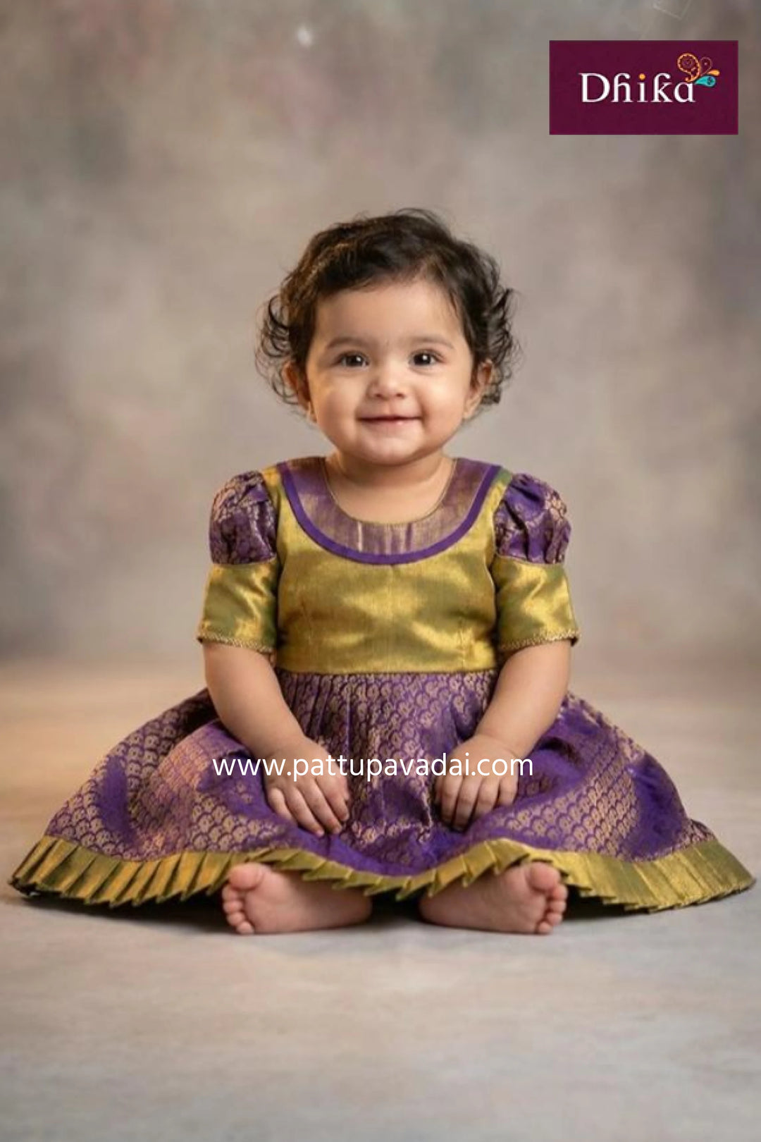 Child wearing a traditional outfit with purple and gold colors, sitting on a plain background.