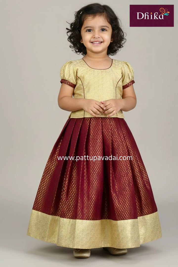 Young girl wearing a traditional outfit with a gold top and maroon skirt, branded 'Dhika'.