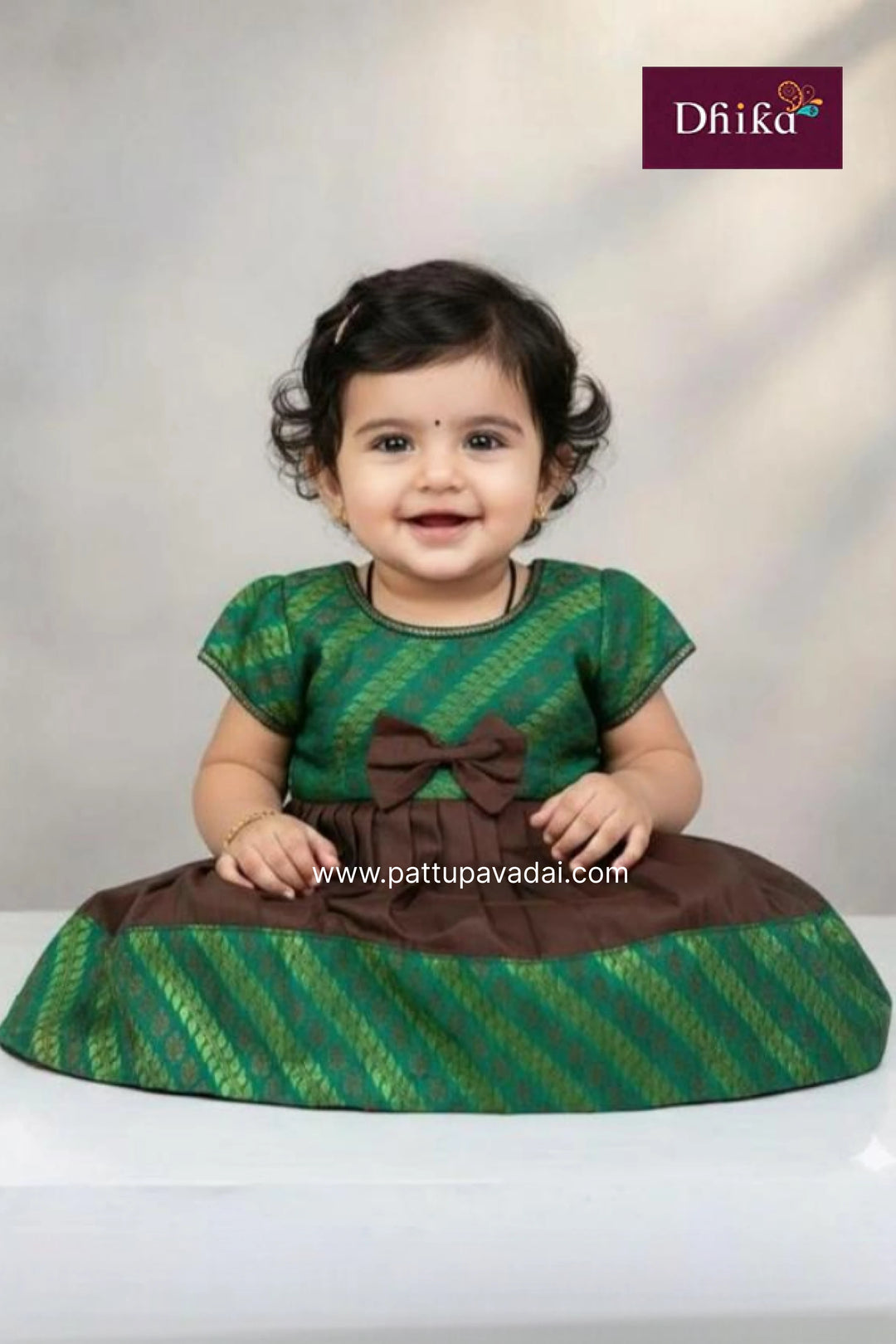 Baby wearing a green and brown traditional outfit with a visible brand logo.