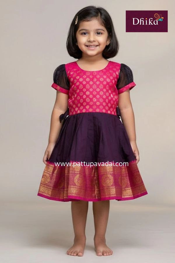Young girl wearing a pink and purple traditional outfit with 'Dhika' branding.