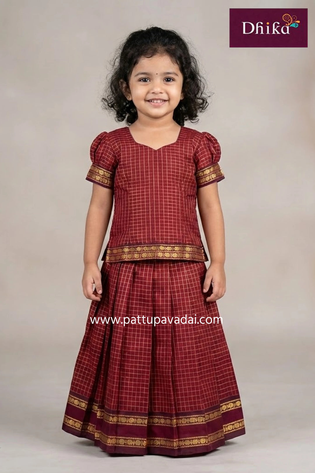 Young girl wearing a traditional red and gold outfit with 'Dhika' branding.