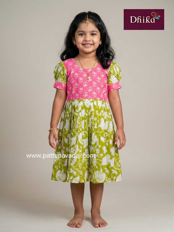 Young girl wearing a pink and green dress with floral patterns, standing against a plain background.