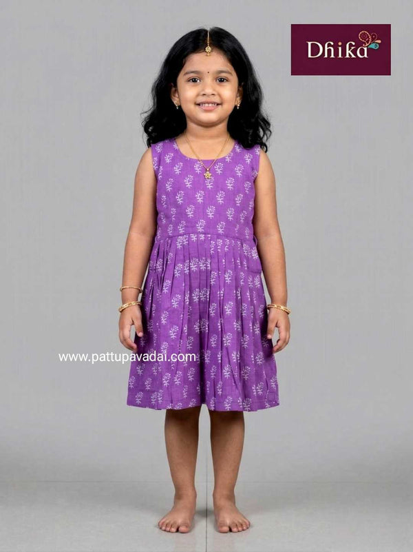 Young girl wearing a purple dress with a floral pattern on a gray background, featuring the brand 'Dhika'.