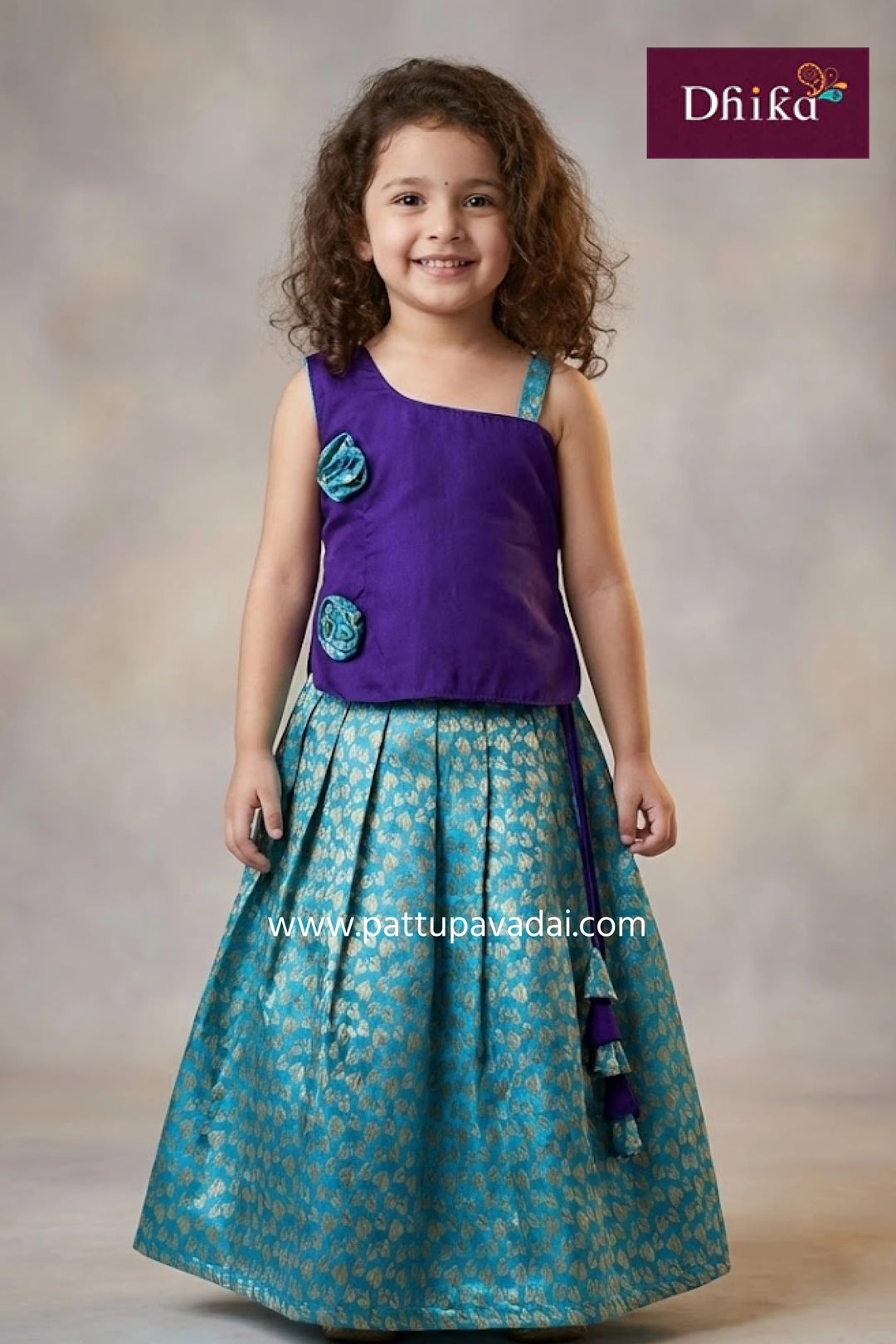 Young girl wearing a purple top and teal skirt with floral patterns, standing against a plain background.