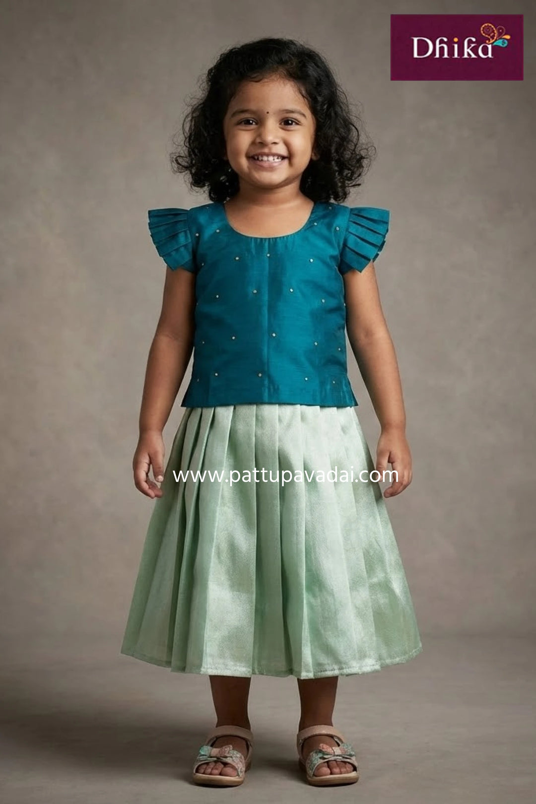 Young girl wearing a teal top and green skirt with 'Dhika' branding.
