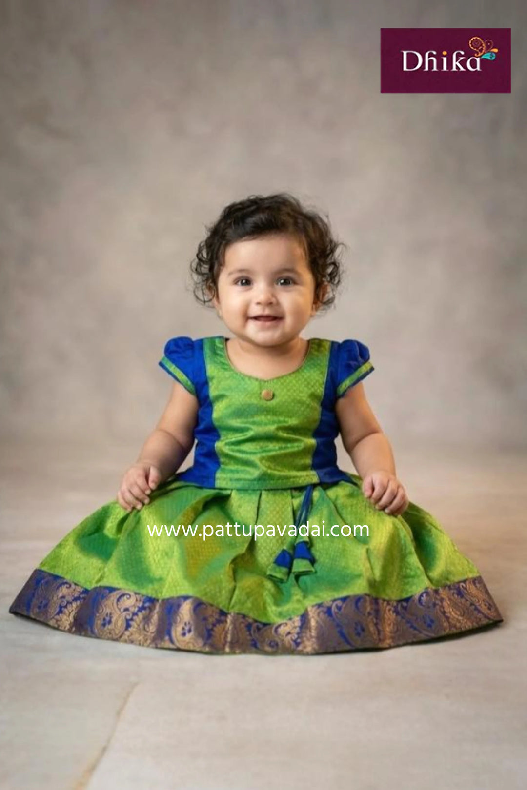 Child wearing a green and blue traditional outfit with 'Dhika' branding.