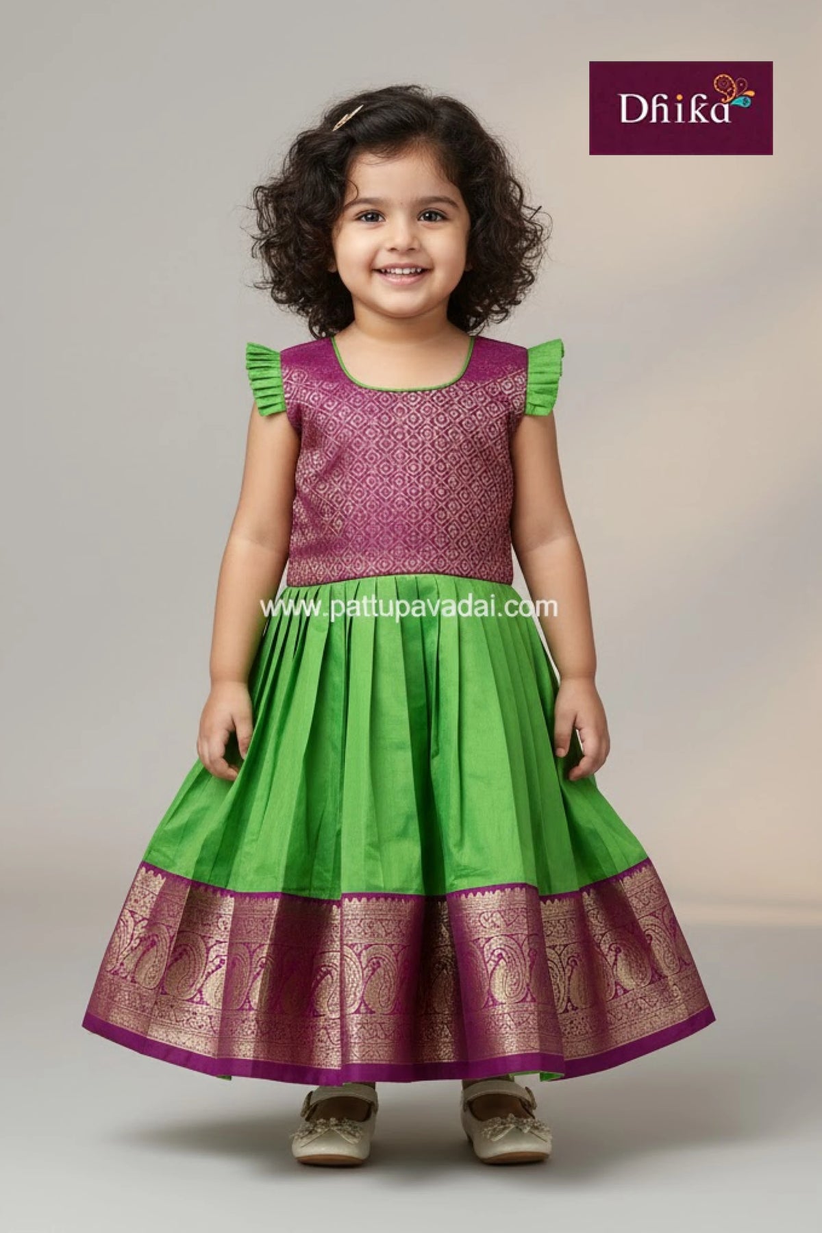 Young girl wearing a green and purple traditional outfit with 'Dhika' branding.