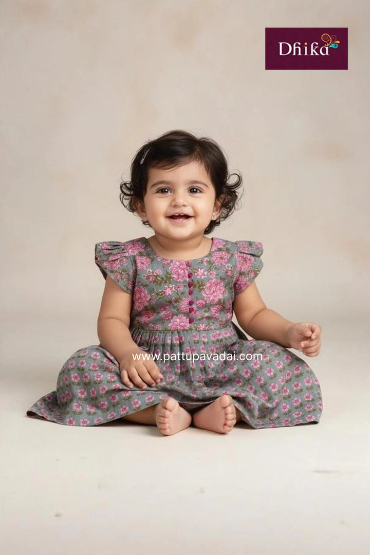 Baby wearing a floral dress sitting on a plain background with Dhika brand logo.