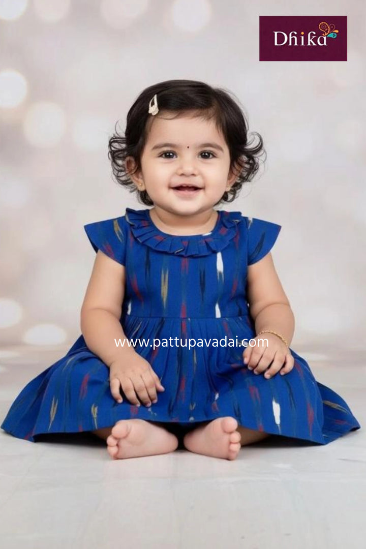 Child wearing a blue dress with ruffled sleeves against a neutral background, featuring the brand 'Dhika'.