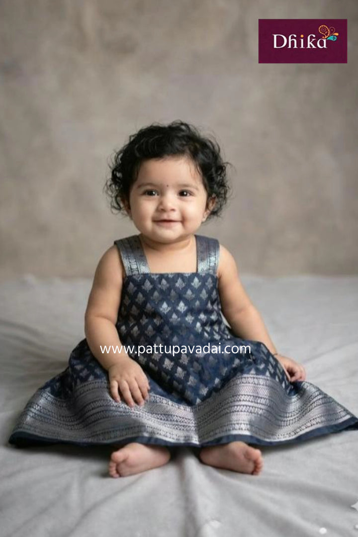 Baby wearing a blue patterned dress sitting on a gray surface with a neutral background