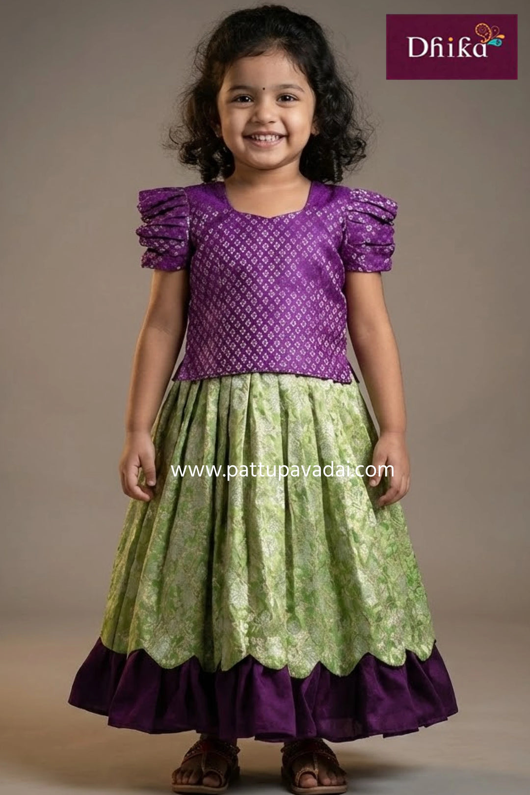 Young girl wearing a purple and green traditional outfit with 'Dhika' branding.
