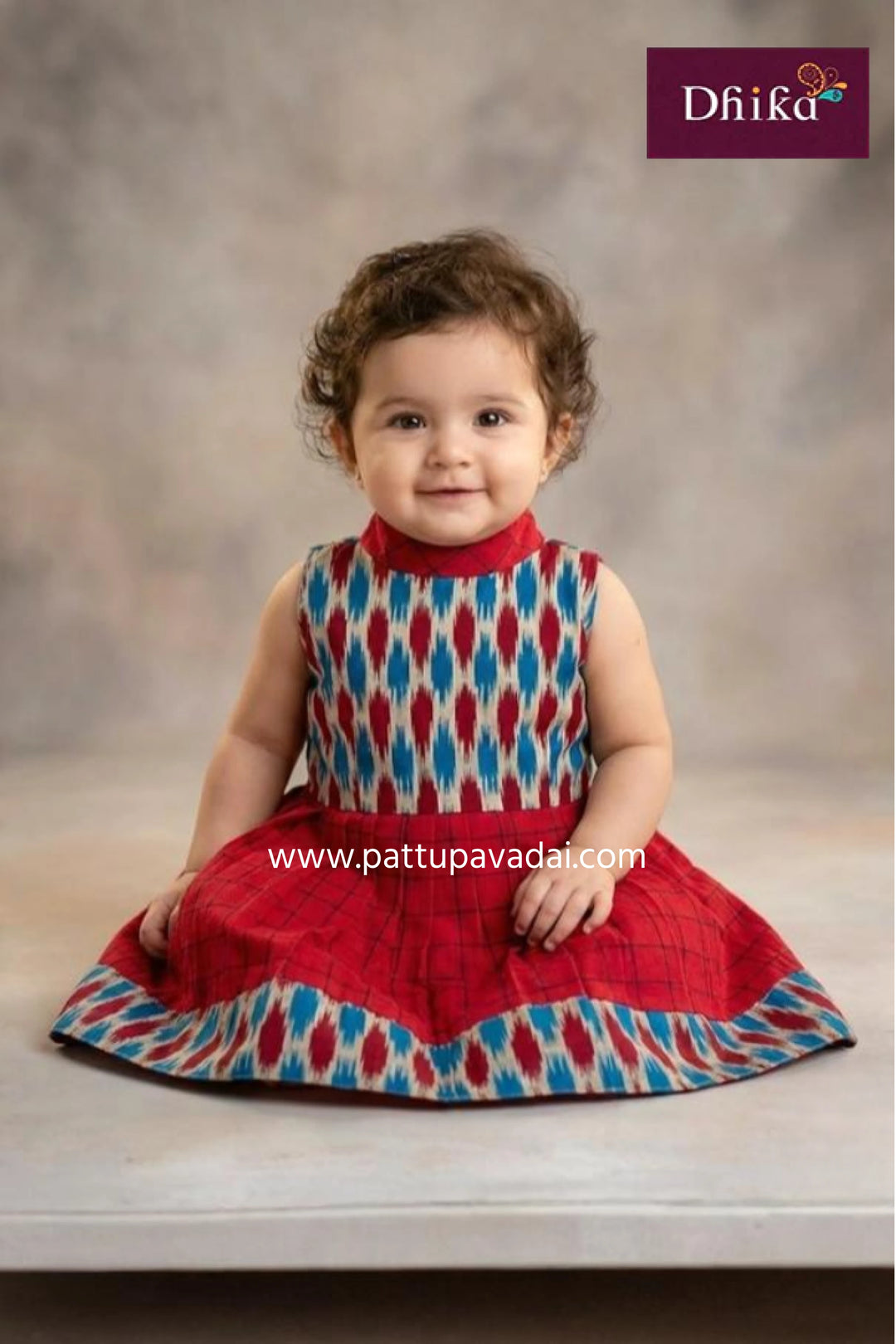 Child wearing a colorful dress with a pattern, sitting on a wooden floor against a neutral background.