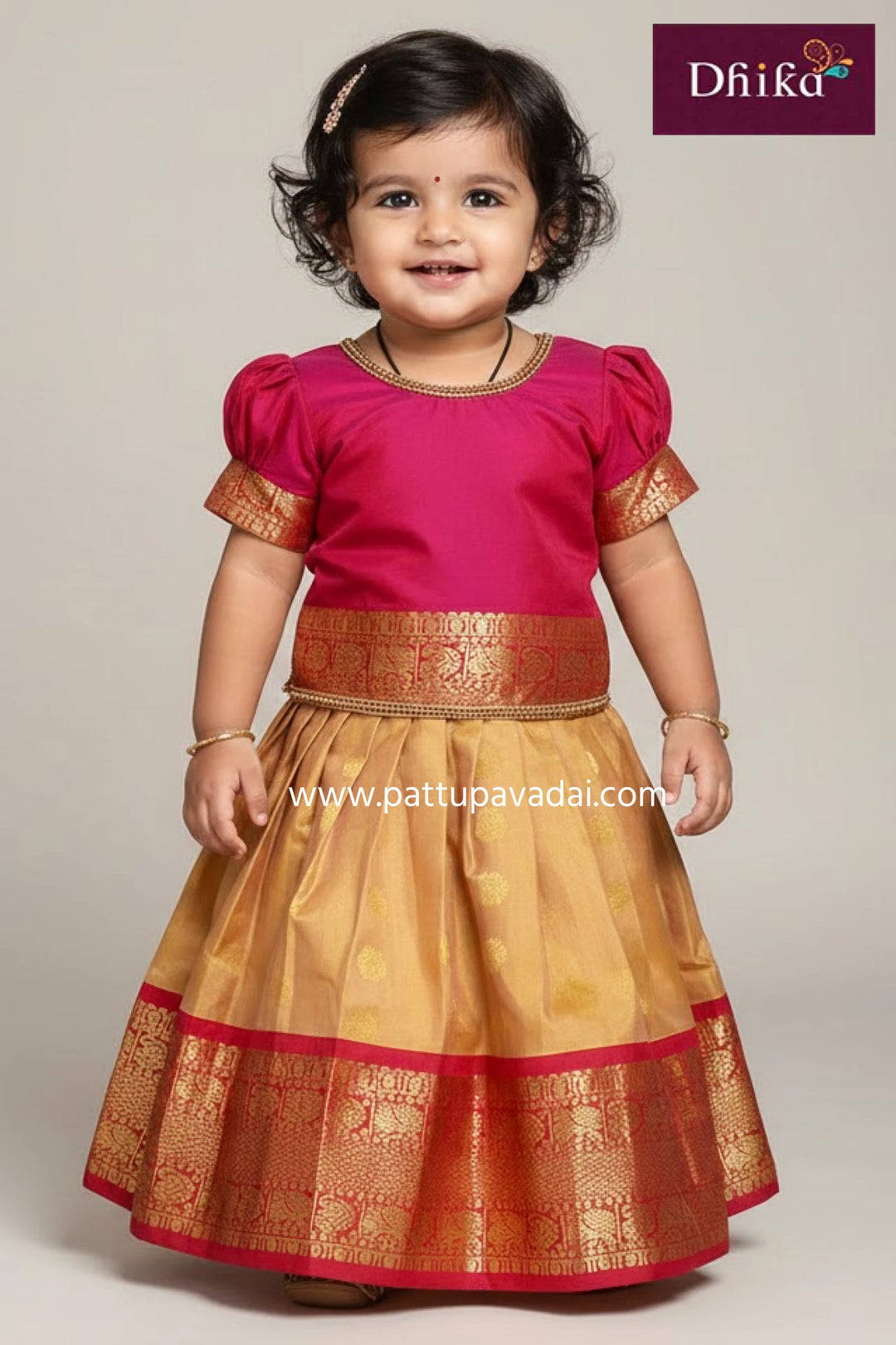 Child wearing a traditional outfit with pink top and gold skirt, brand 'Dhika' visible