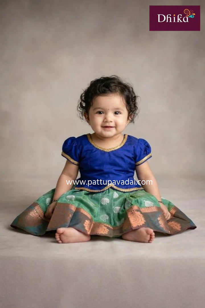 Young girl wearing a traditional blue and silver dress with pink hem, branded 'Dhika'.