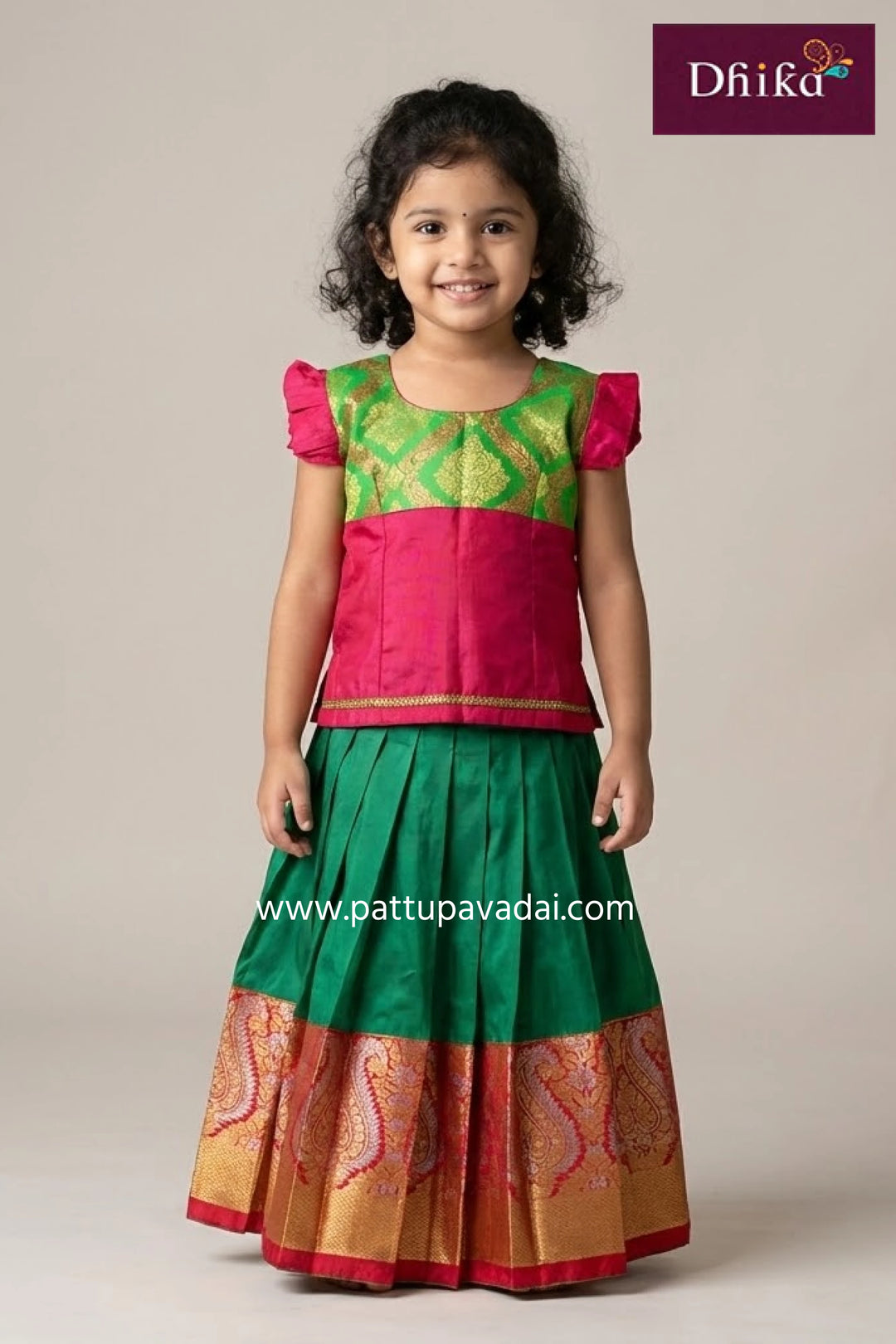 Child wearing a green and pink traditional outfit with 'Dhika' branding.