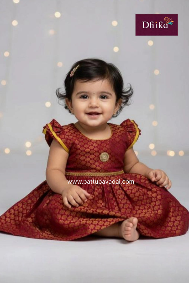 Baby in a red dress with yellow trim sitting on a light gray background, Dhiika brand visible.