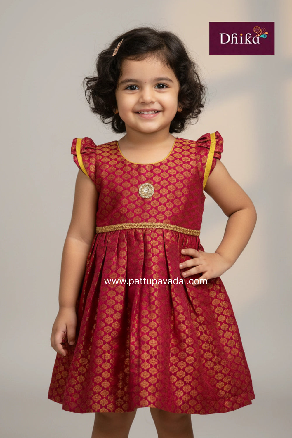 Young girl wearing a red dress with yellow accents, smiling against a plain background.