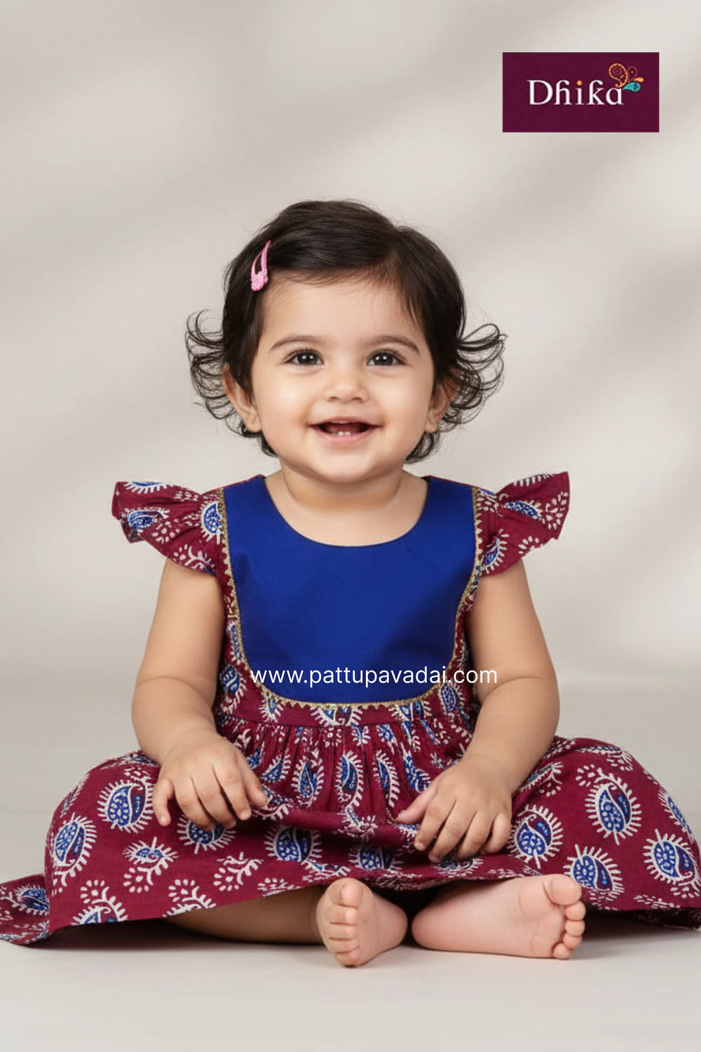 Child wearing a blue and maroon dress with a visible brand logo on a light background