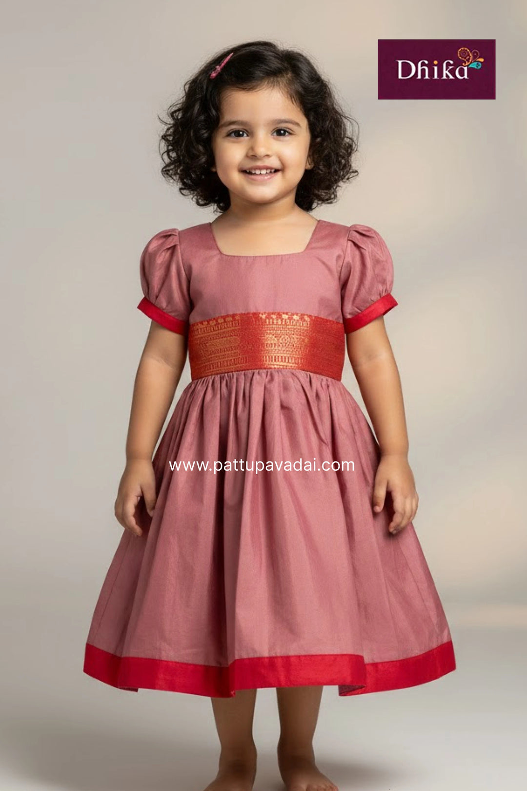 Young girl wearing a pink dress with red accents, standing against a plain background.