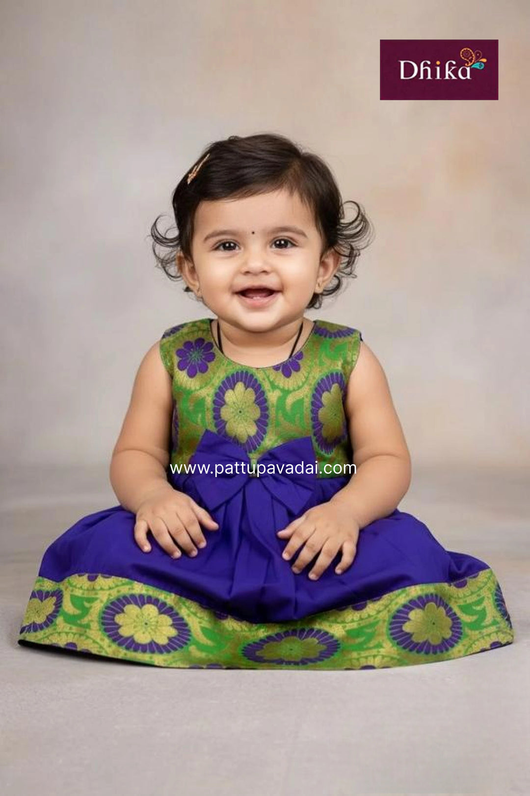Baby wearing a green and purple traditional outfit with Dhiika branding.