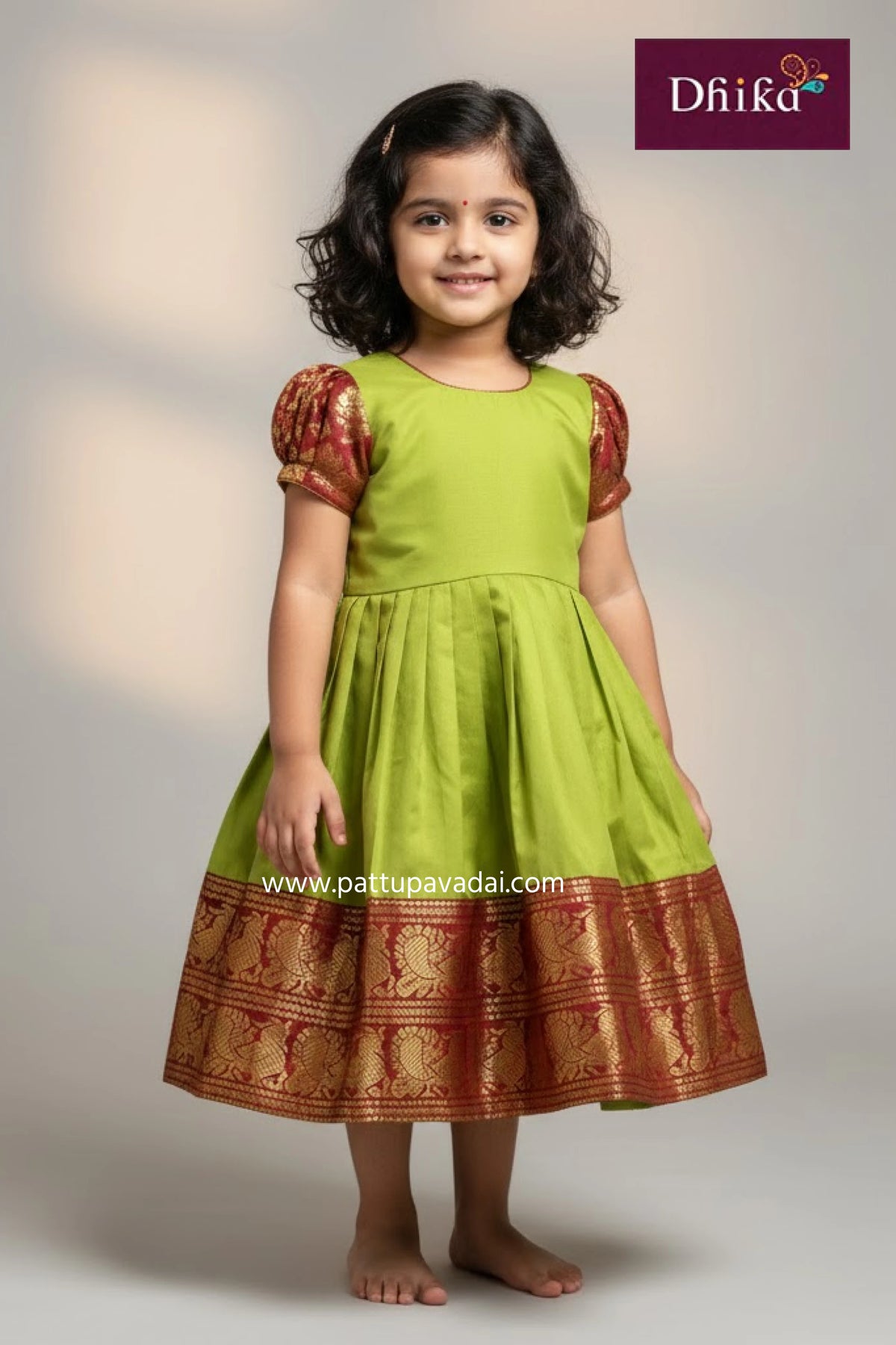 Young girl wearing a green and brown traditional dress with 'Dhika' branding.