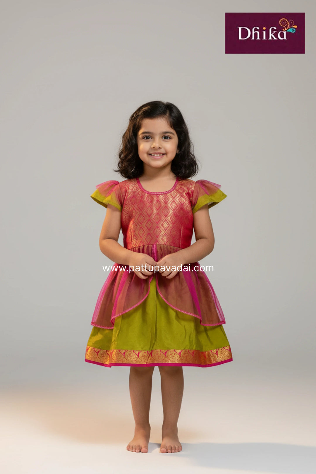 Young girl wearing a pink and green traditional outfit with 'Dhika' branding.