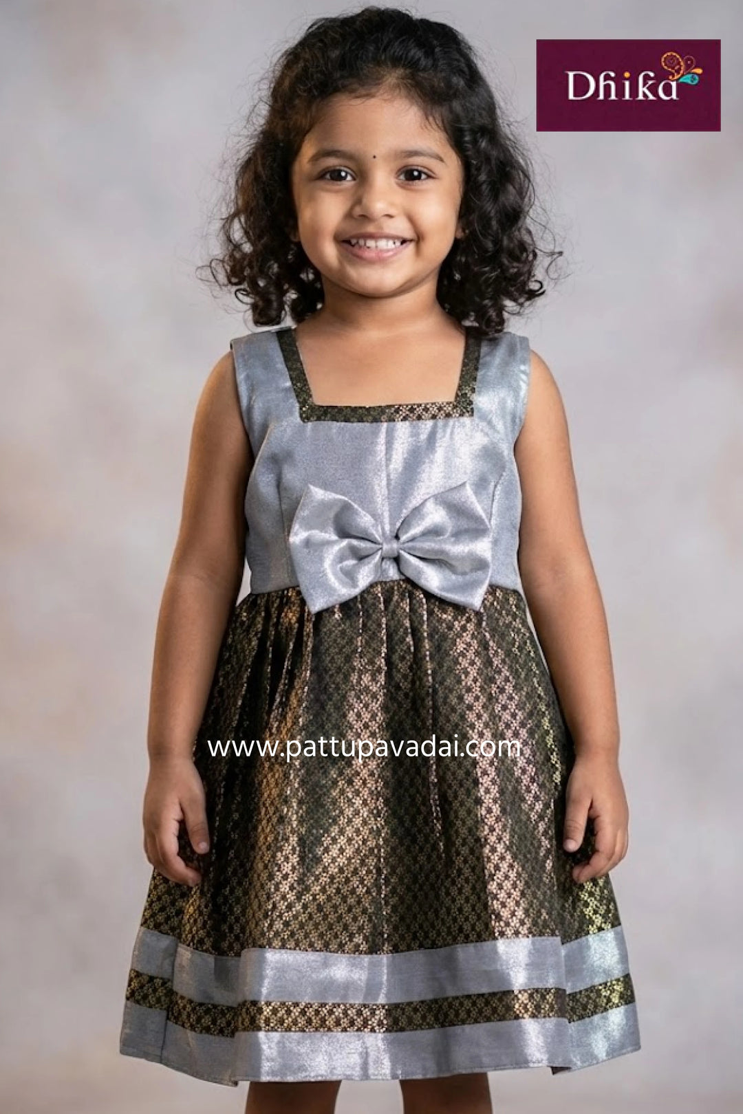 Young girl wearing a silver and brown dress with a bow, branded 'Dhika'.