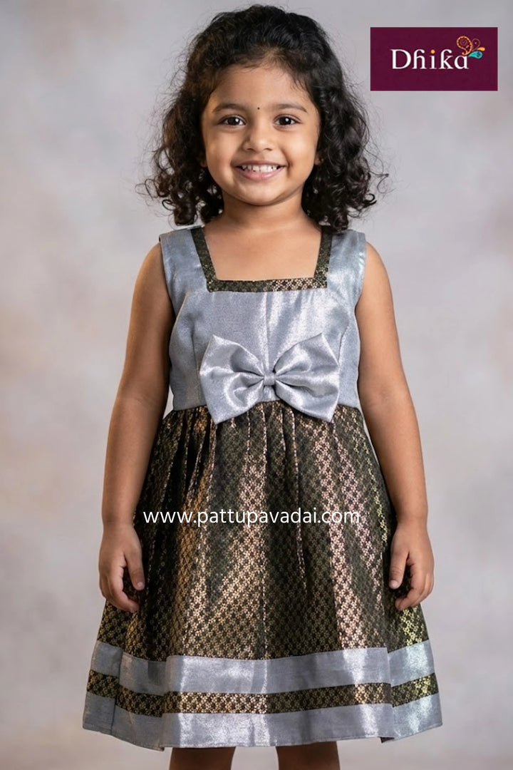 Young girl wearing a silver and brown dress with a bow, branded 'Dhika'.
