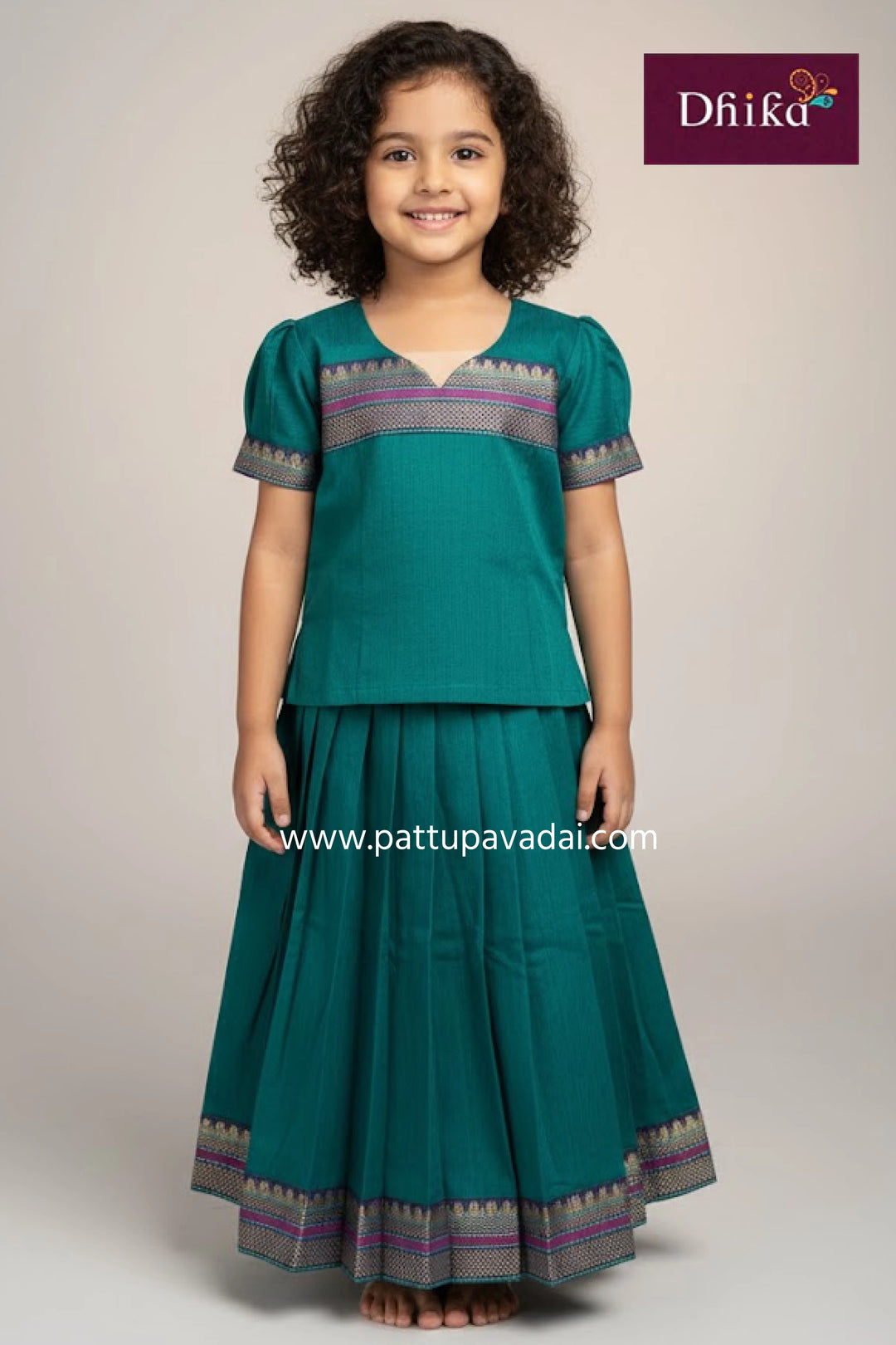 Young girl wearing a teal traditional outfit with a matching skirt, standing against a plain background.