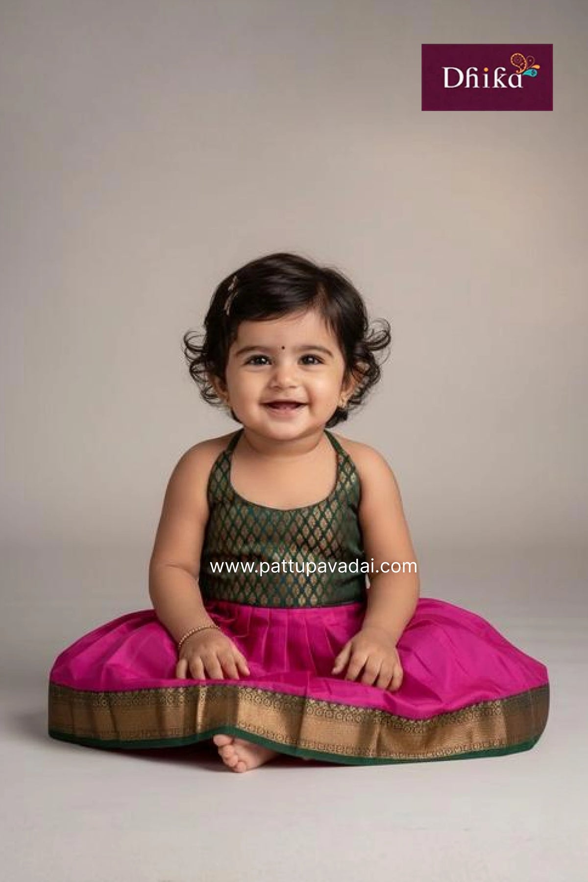 Child wearing a traditional outfit with a pink skirt and green top, sitting on a light gray background.