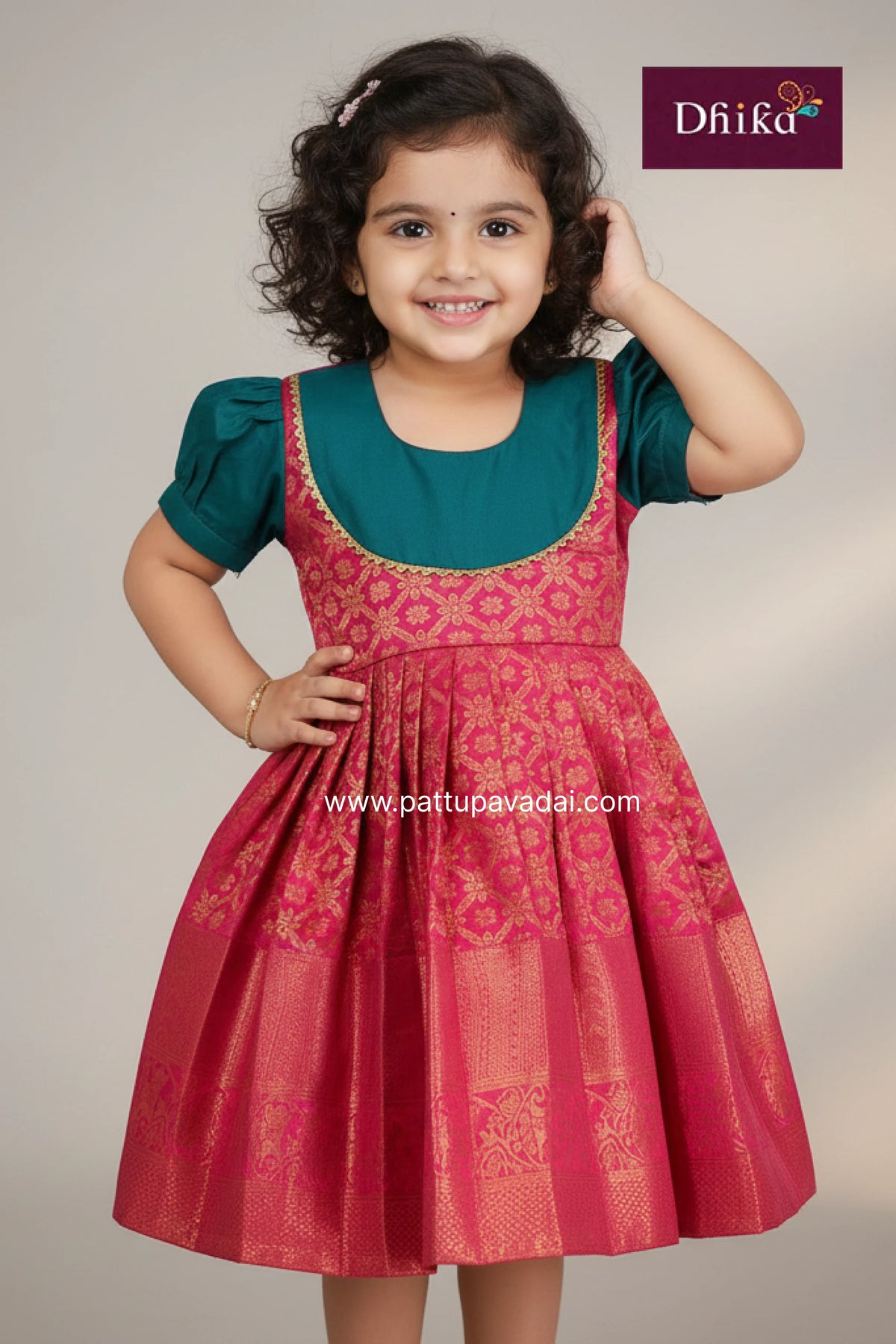 Young girl wearing a red and green traditional dress with 'Dhika' branding.