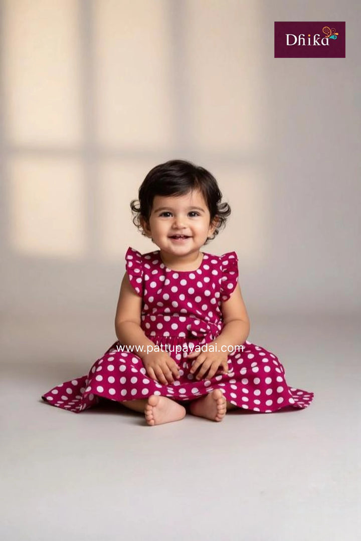 Child wearing a pink polka dot dress sitting on a light background with 'Dhink' branding.