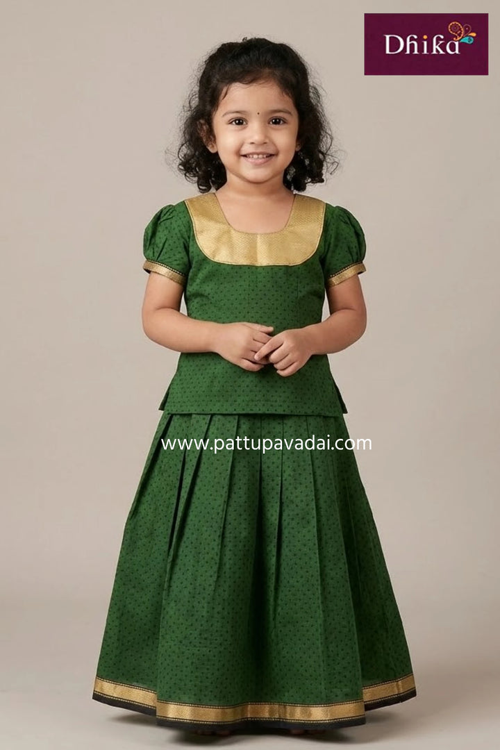 Young girl wearing a green traditional outfit with gold accents, standing against a plain background.