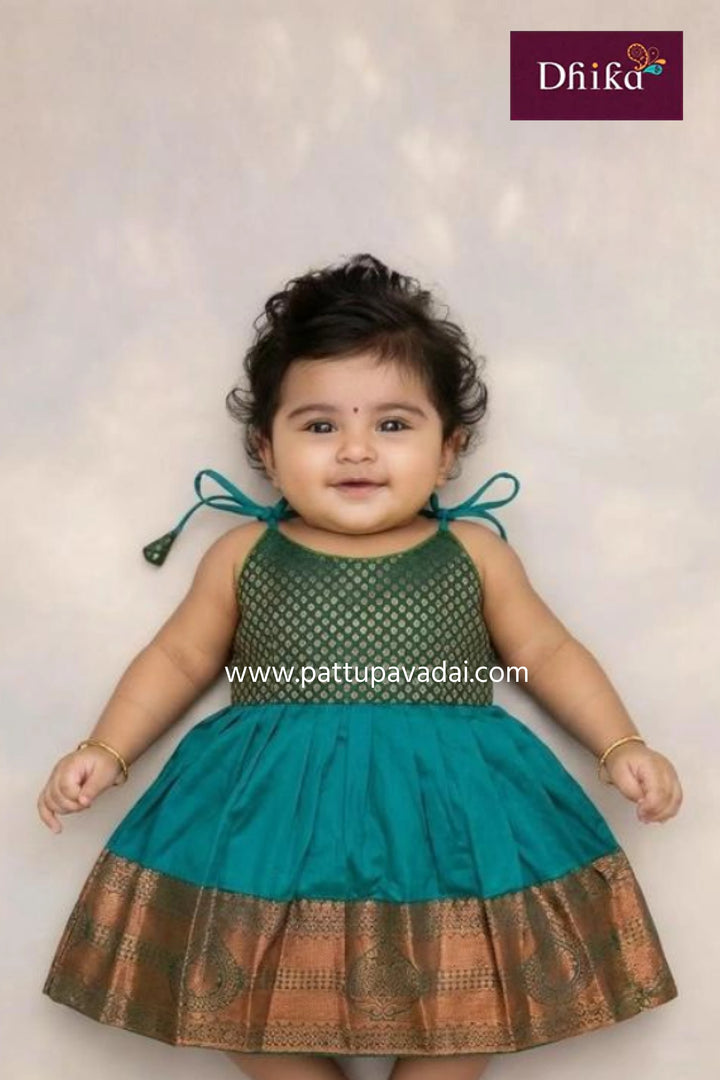 Baby wearing a green and teal traditional outfit with 'Dhika' branding.