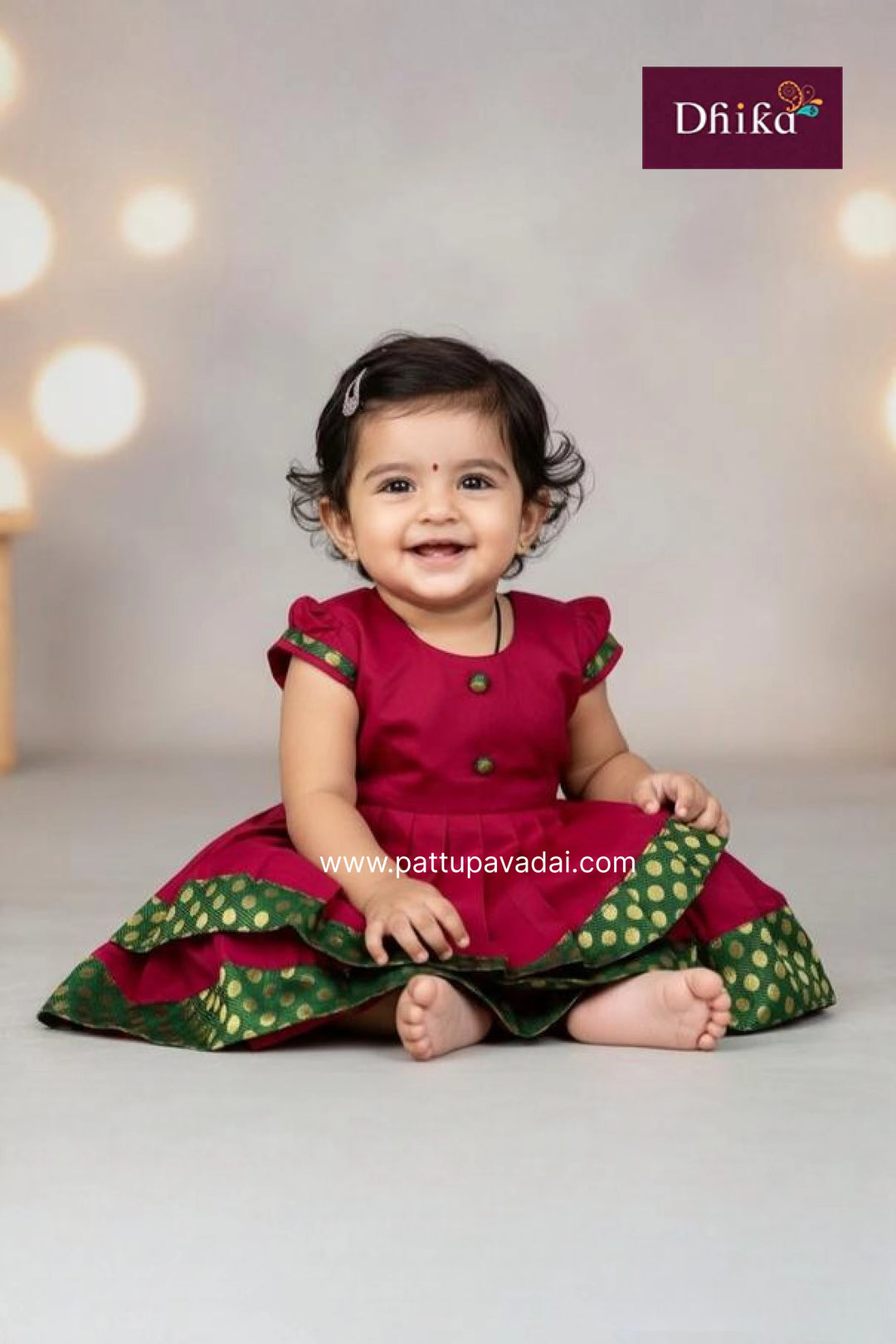 Baby wearing a red and green traditional outfit with Dhiika branding.