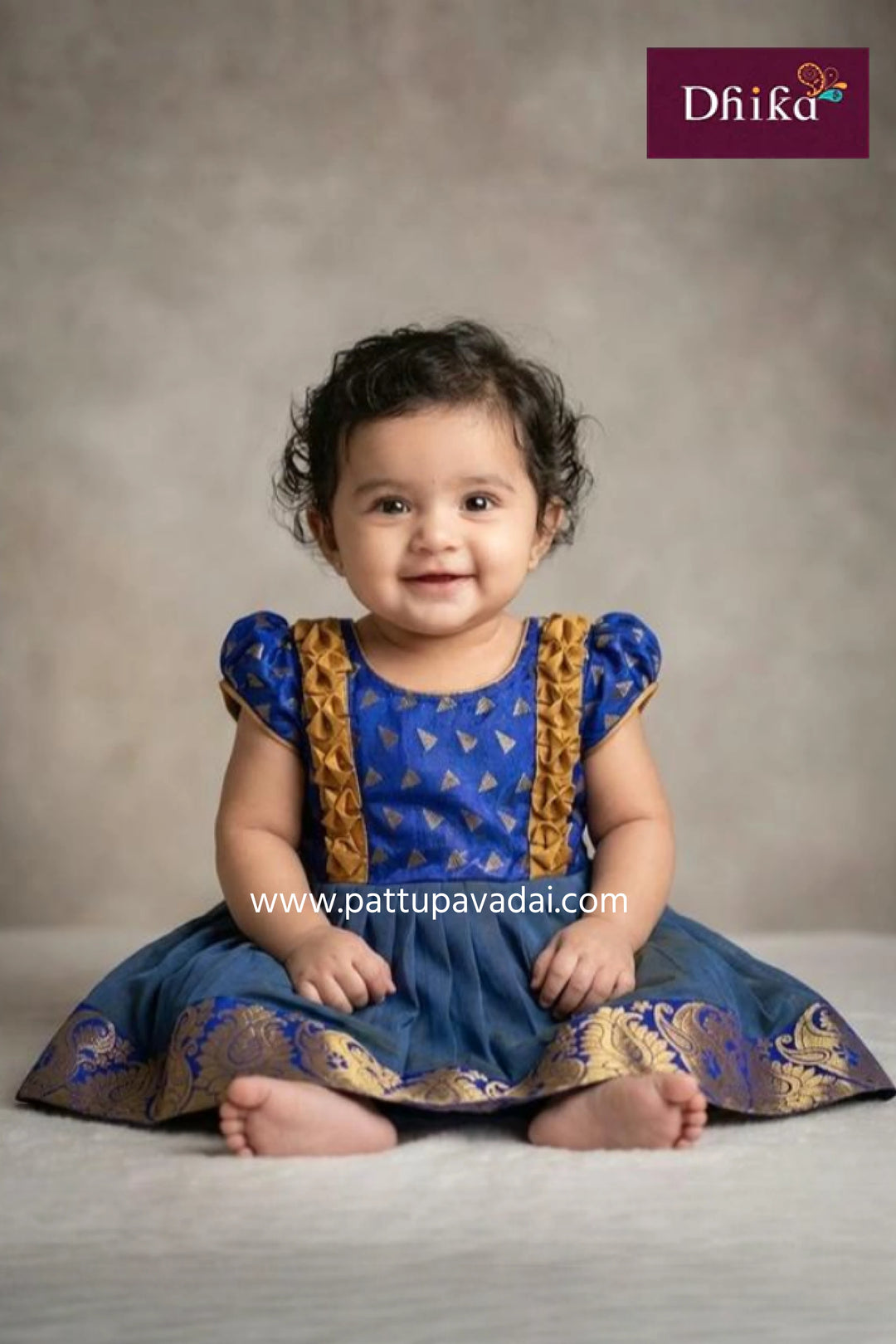 Baby wearing a blue and gold traditional outfit with 'Dhika' branding.