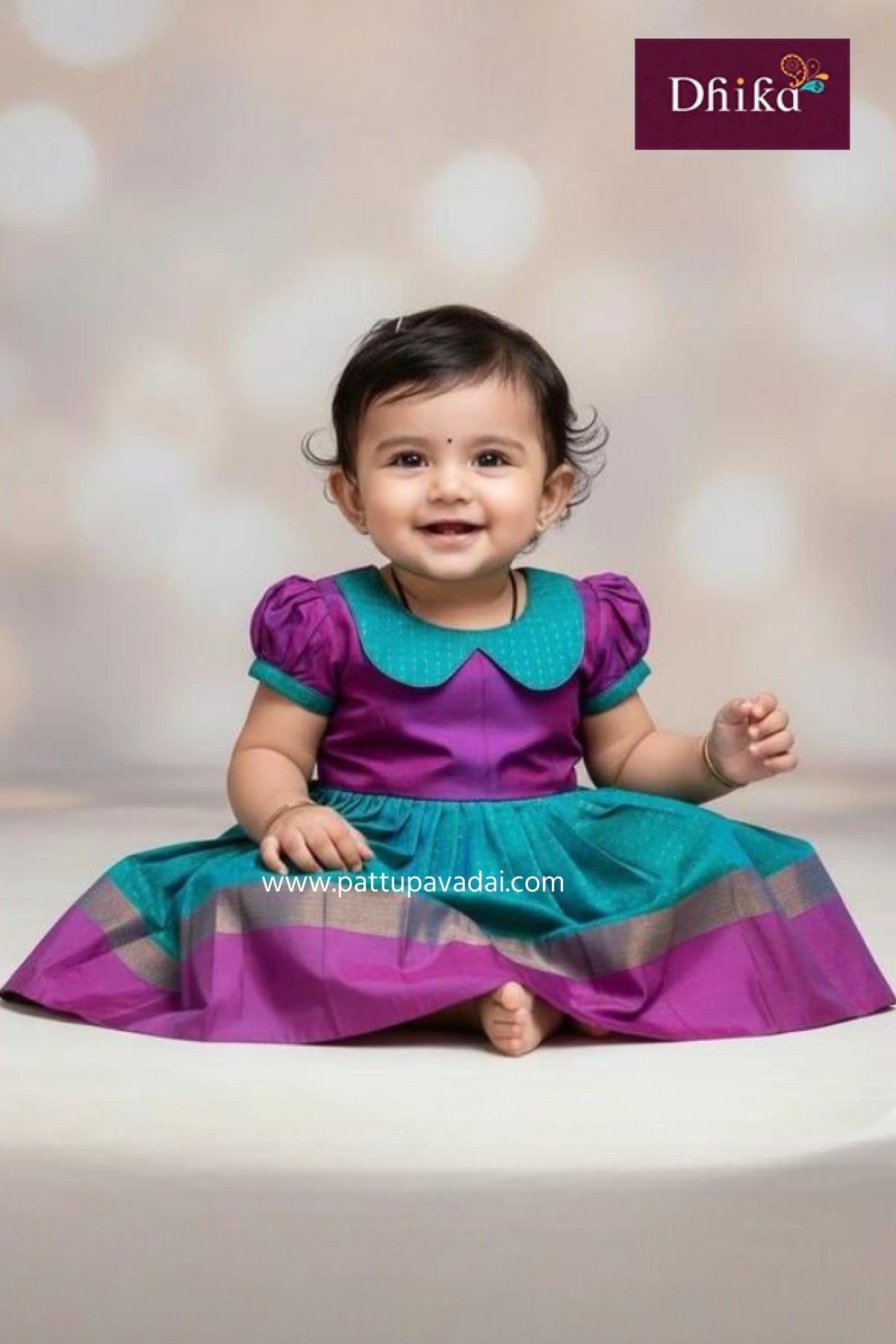 Baby wearing a purple and teal dress with a blurred background