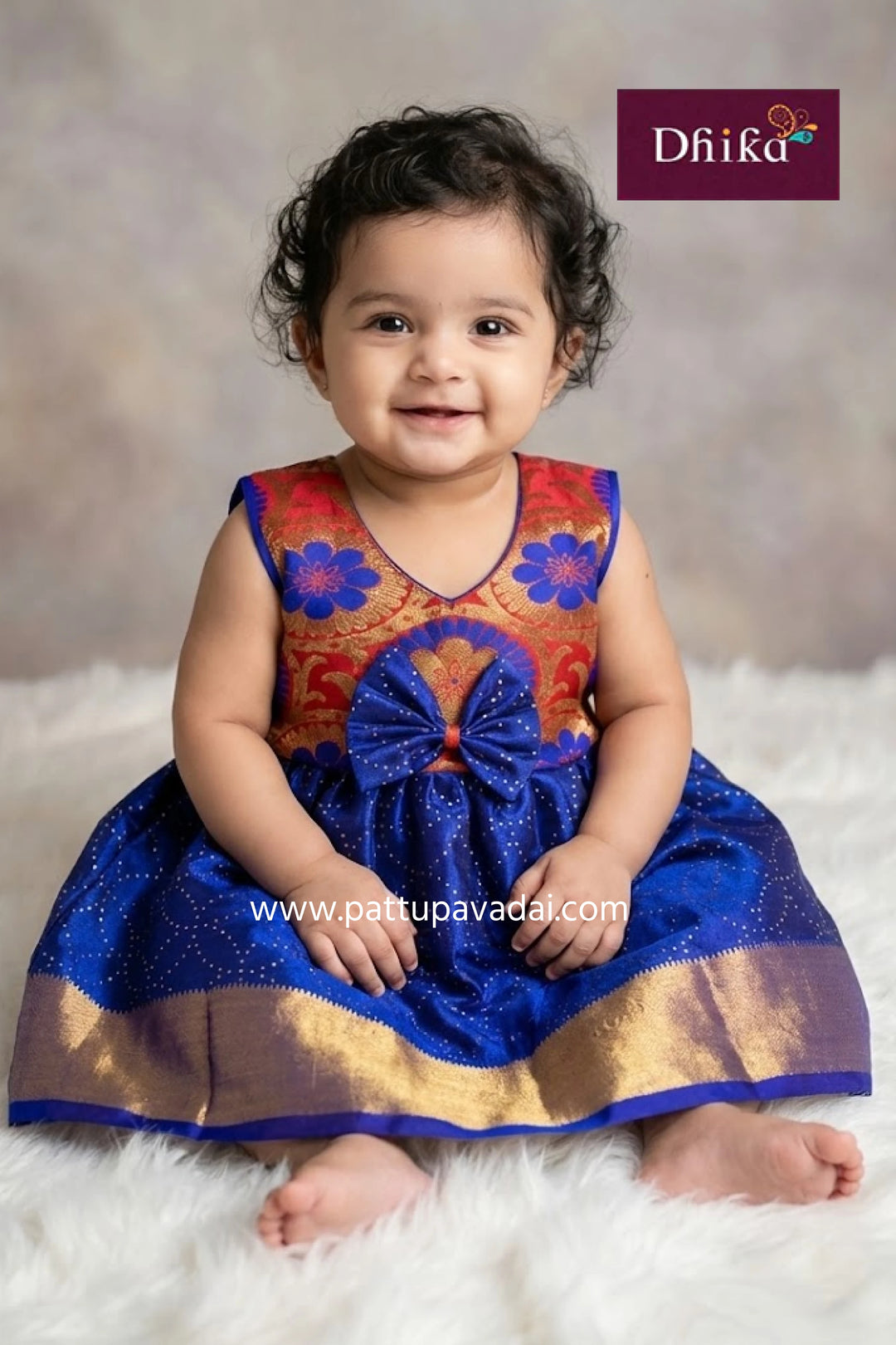 Child wearing a colorful traditional outfit with a blue skirt on a white surface, branded 'Dhika'.