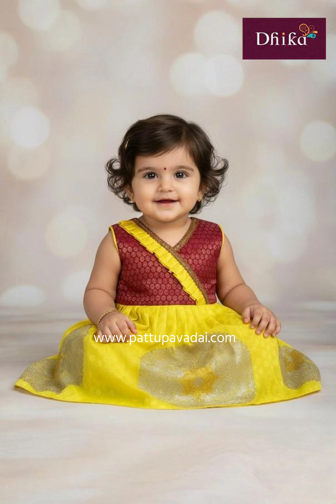 Baby in a yellow and maroon traditional outfit with 'Dhika' branding.
